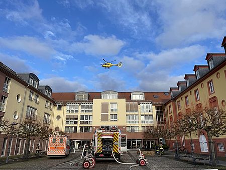 Rettungswagen, Löschfahrzeug stehen vor dem Seniorenheim, darüber schwebt ein Rettungshubschrauber