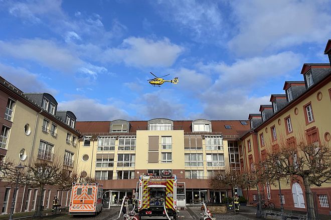 Rettungswagen, Löschfahrzeug stehen vor dem Seniorenheim, darüber schwebt ein Rettungshubschrauber